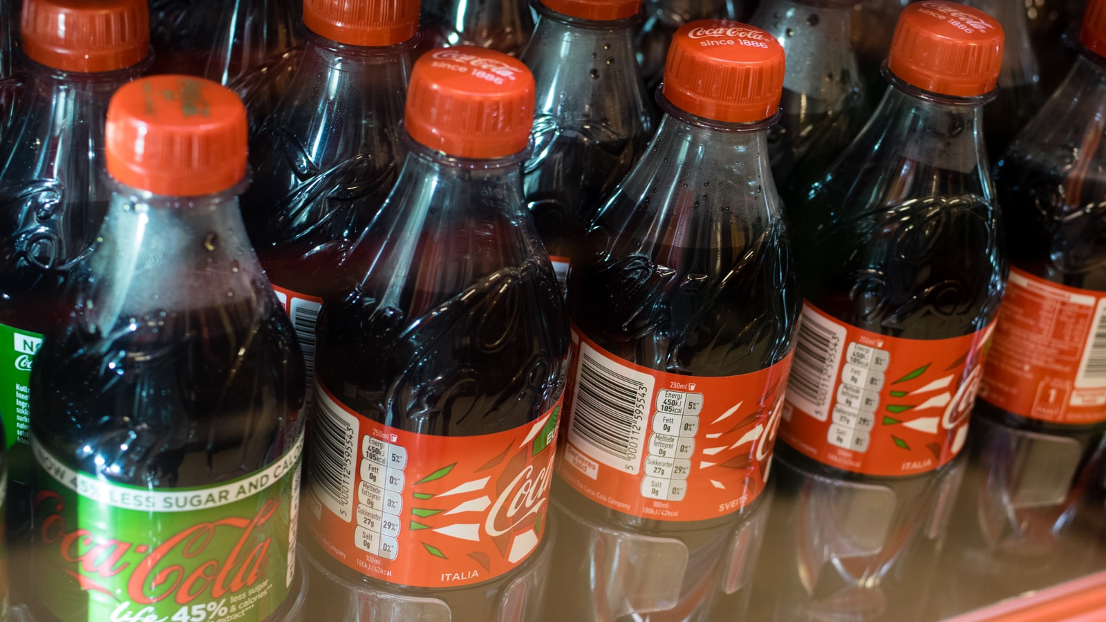 Rows of Coca-Cola bottles inside a retail cooler.