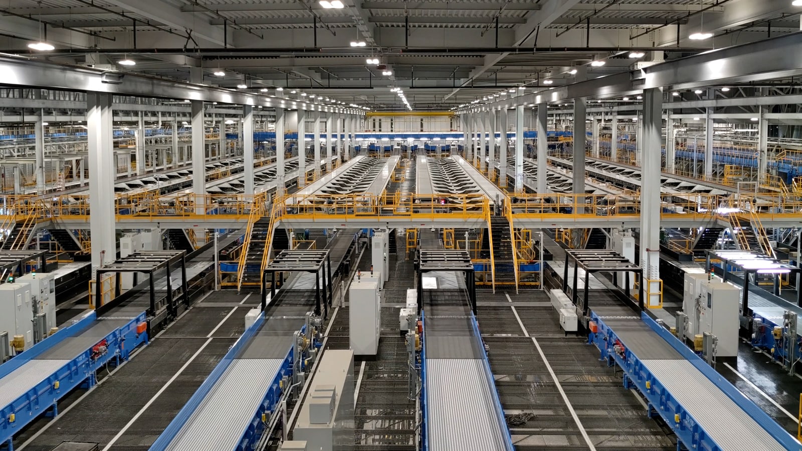 Wide documentary view inside a modern FedEx parcel sort hub with conveyors, workers, packages, and delivery vehicles.