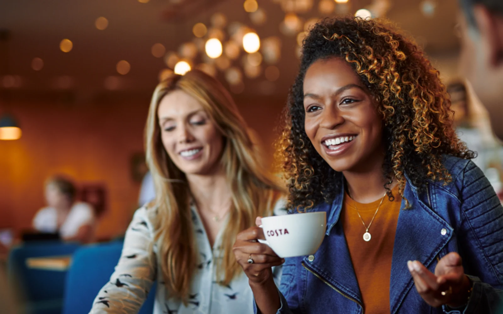 Costa Coffee café scene with customers holding branded cups in warm burgundy and amber surroundings.