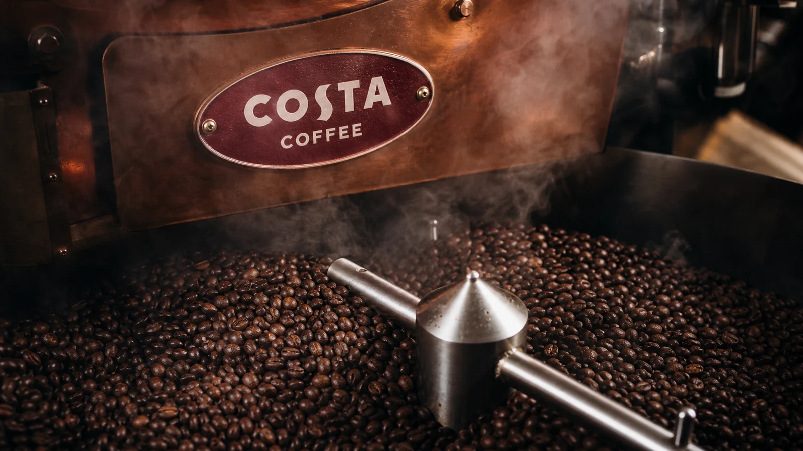 Copper Costa Coffee roaster moving glossy beans beneath a burgundy Costa badge.