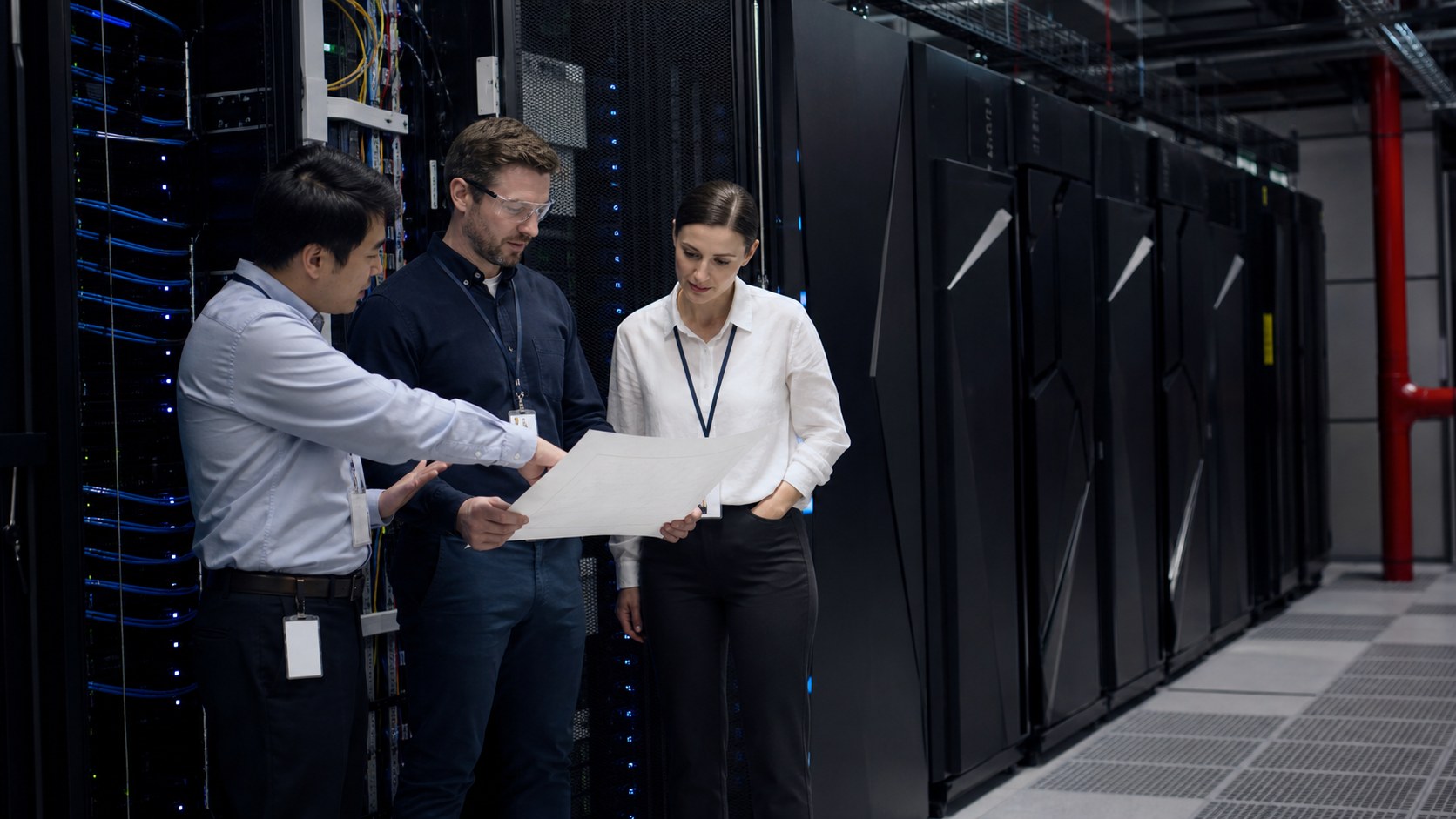 Infrastructure engineers reviewing a rack plan beside enterprise compute cabinets and network fabric.