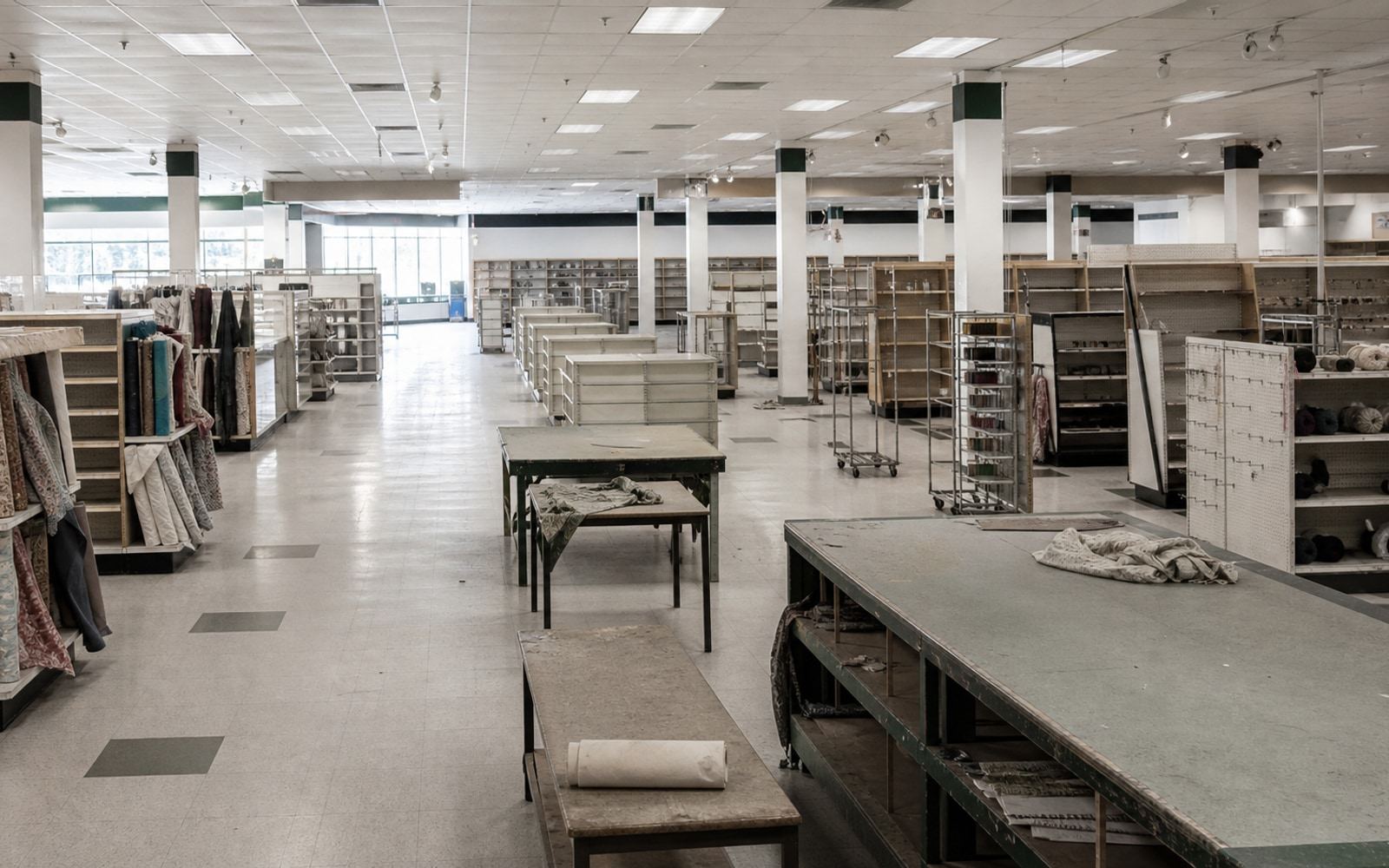 A largely emptied fabric and craft superstore with cutting tables and sparse shelves after liquidation.