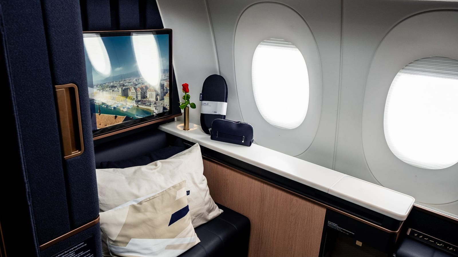 Lufthansa Allegris First Class single suite with navy upholstery, privacy wall, monitor, and cabin window.