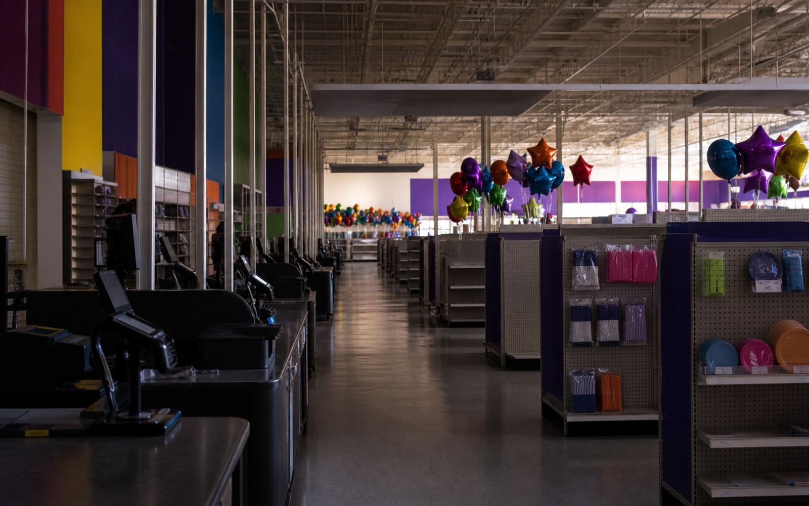 A darkened party-supply superstore with closed checkouts, partly cleared aisles, and unbranded balloon bouquets after liquidation.