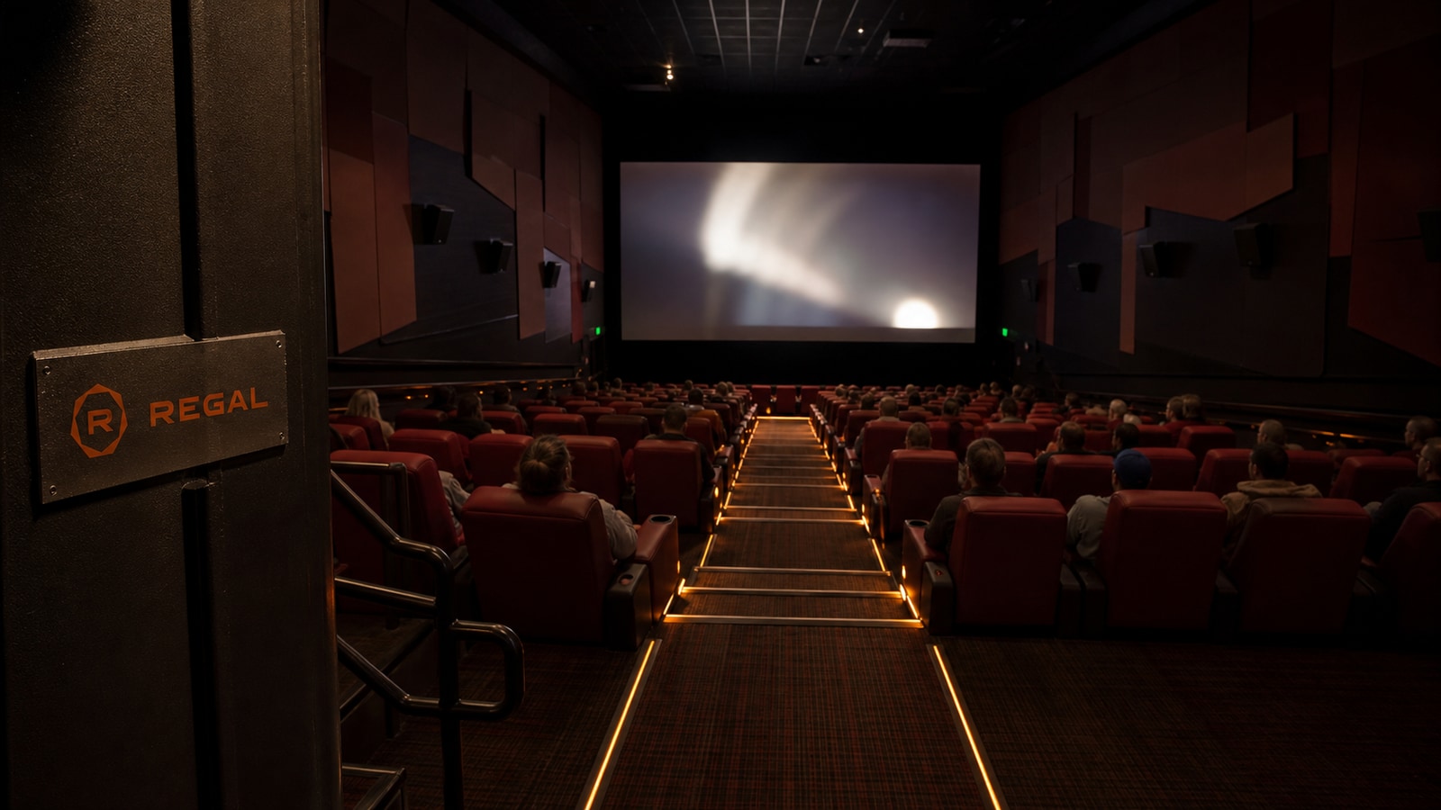 A modern Regal auditorium during the 2022 attendance recovery with scattered guests, red recliners, orange aisle lights, and a small current mark.