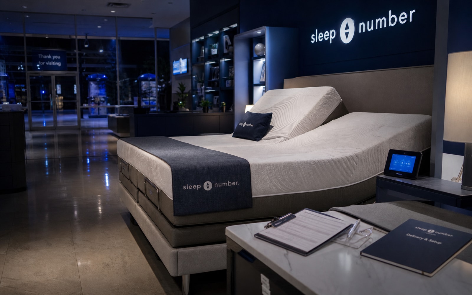 A Sleep Number smart-bed retail showroom with adjustable bed, app tablet, delivery documents, and sale-process files.
