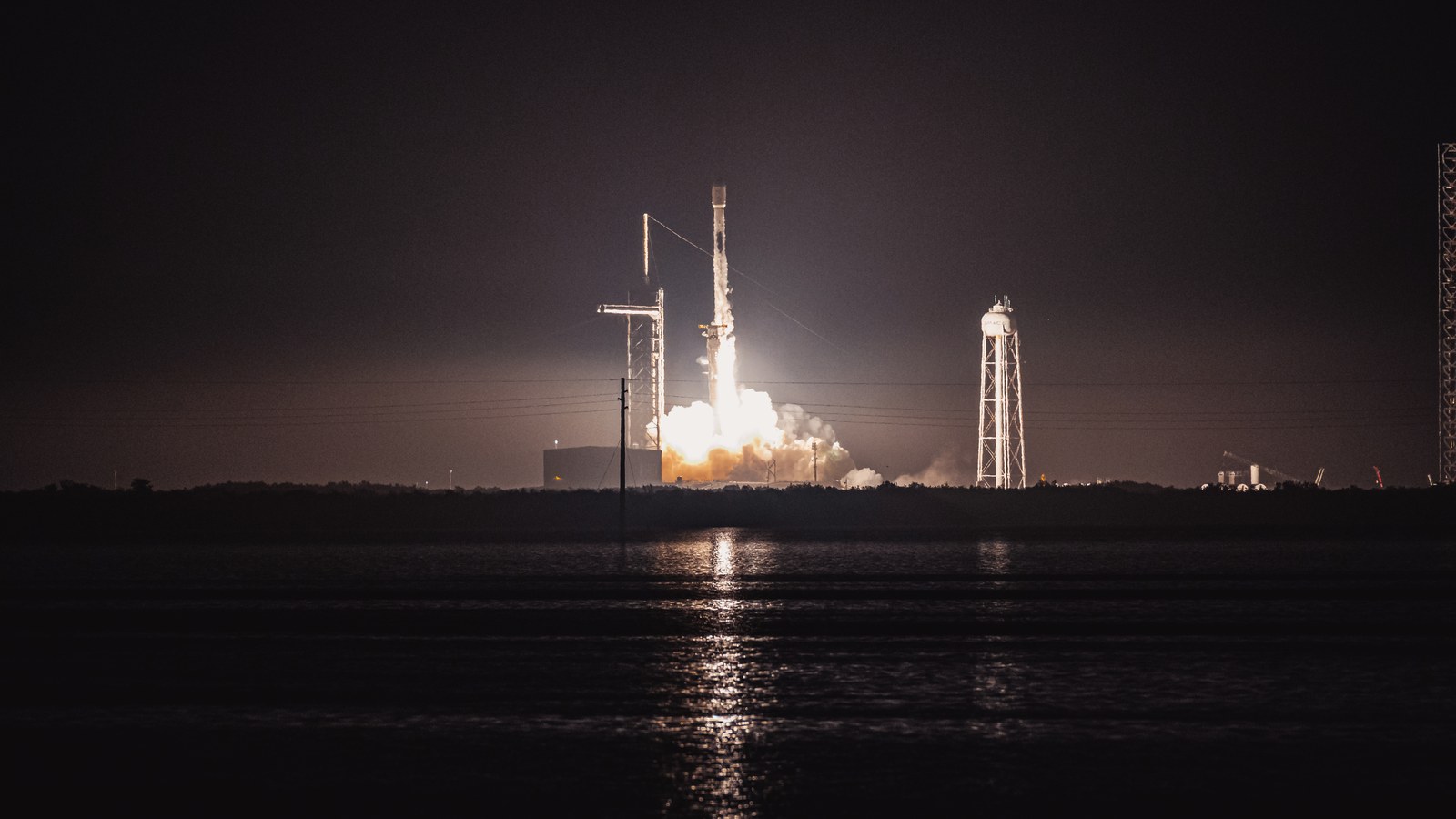Falcon 9 night launch for a Starlink mission with the launch tower, flame, and reusable rocket system visible.