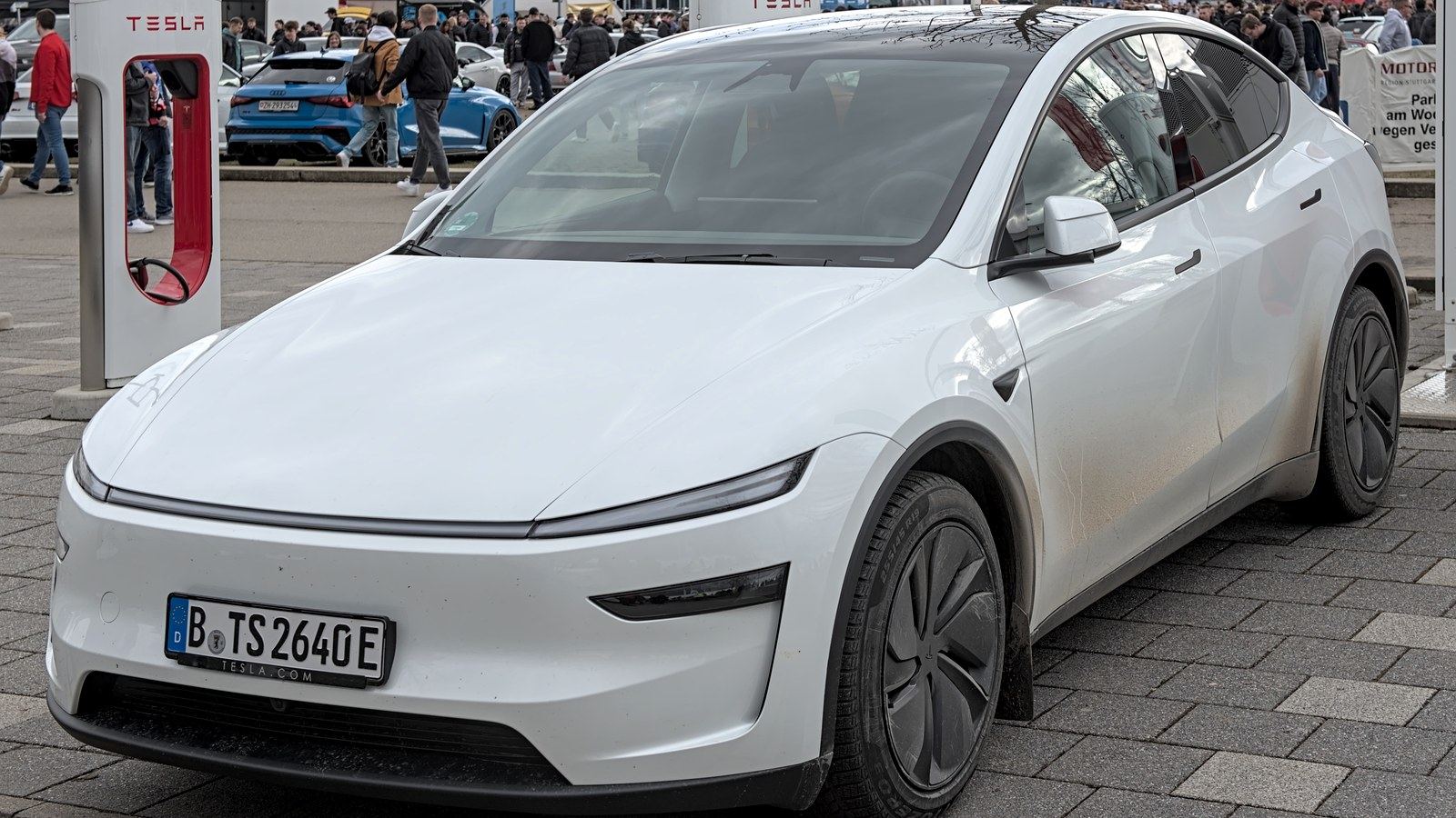 Current white Tesla Model Y photographed beside Tesla charging infrastructure.
