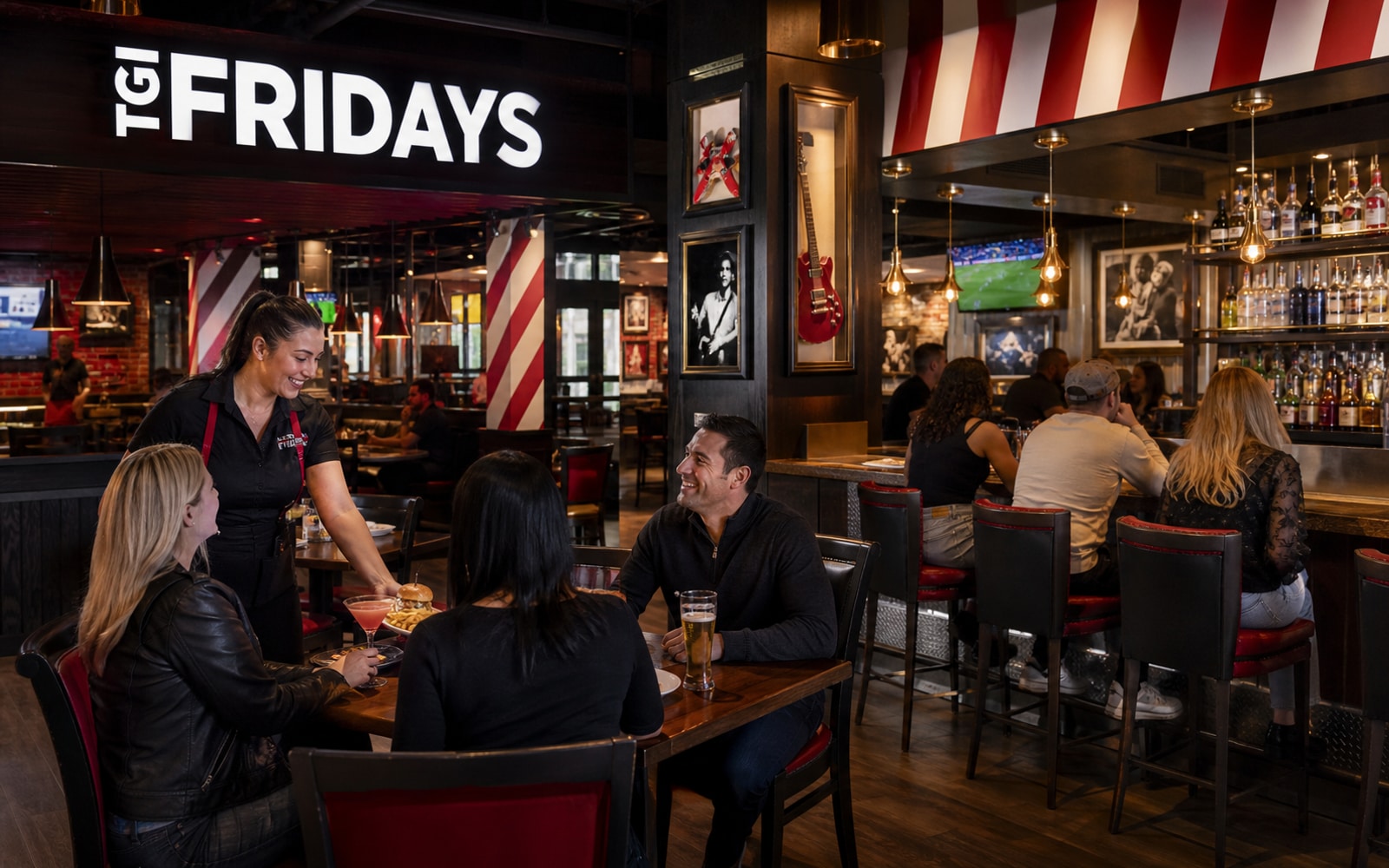 A lively active TGI Fridays bar-and-grill with guests, staff, current striped identity, and realistic restaurant proportions.