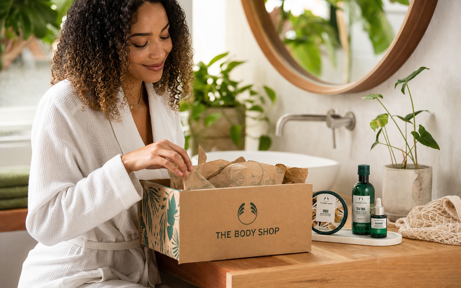 A U.S. customer opening a current The Body Shop ecommerce parcel beside a bathroom vanity and recognizable body-care products.