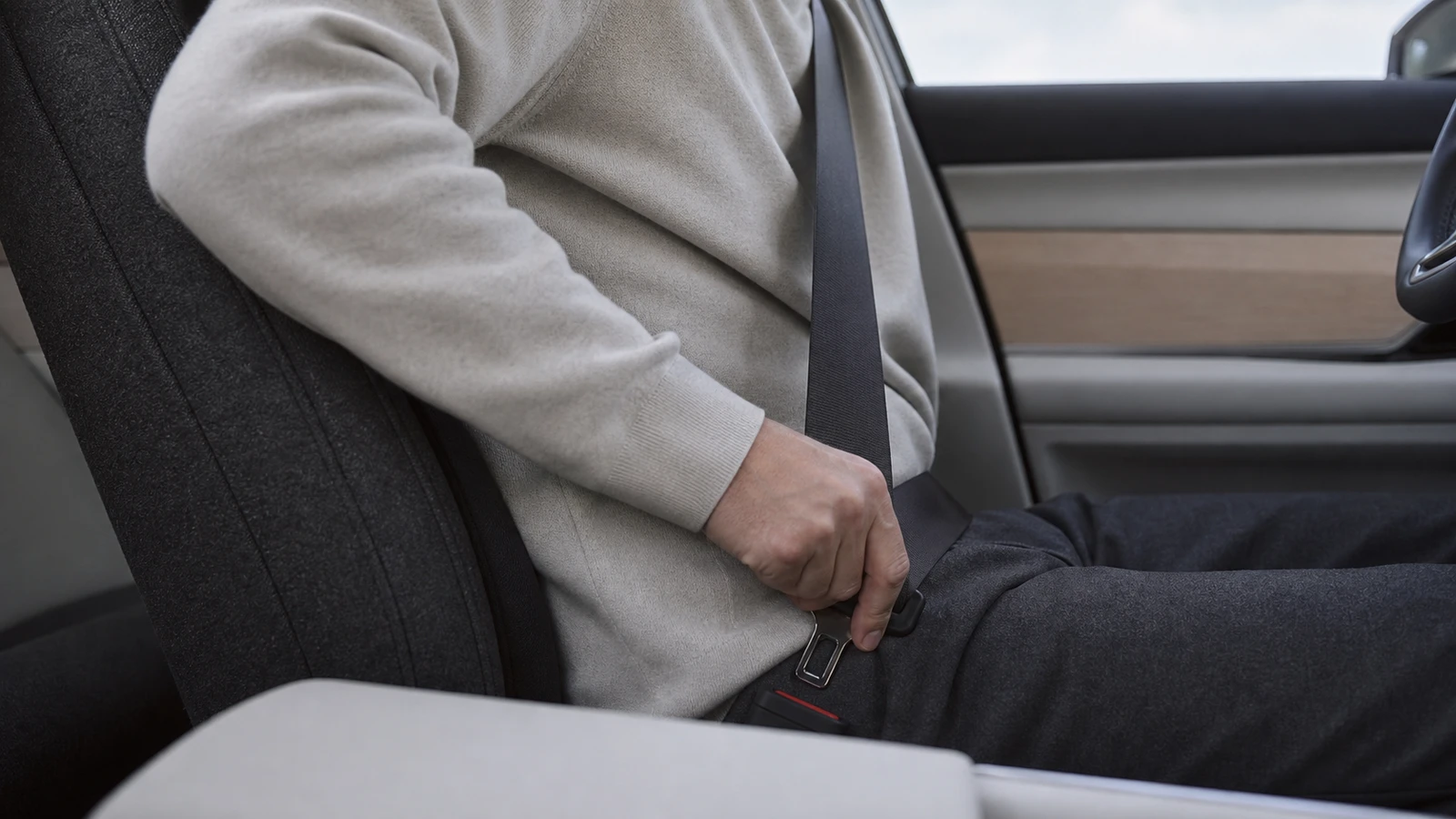 Logo-free close view of a driver fastening a three-point seat belt in a restrained Scandinavian cabin.