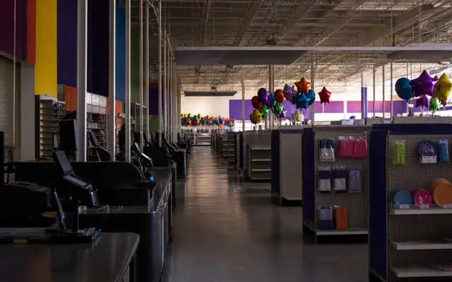 A darkened party-supply superstore with closed checkouts, partly cleared aisles, and unbranded balloon bouquets after liquidation.