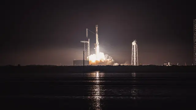 Falcon 9 night launch for a Starlink mission with the launch tower, flame, and reusable rocket system visible.